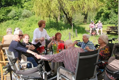 Zu sehen ist eine Gruppe von Bewohnerinnen und Bewohnern, die gemeinsam an einem Tisch im Garten sitzen und Hand in Hand schunkeln. 